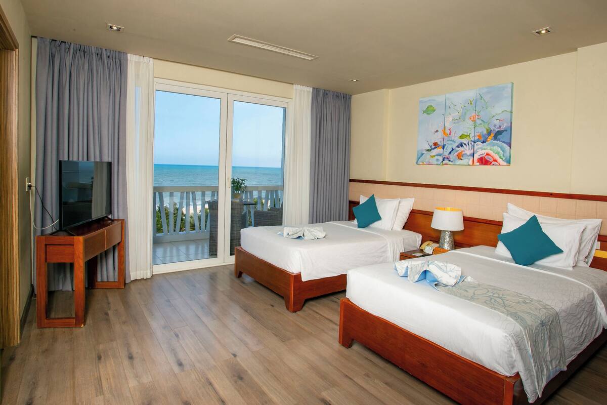 A hotel room with two beds, a TV, and a balcony with a view of the sea.