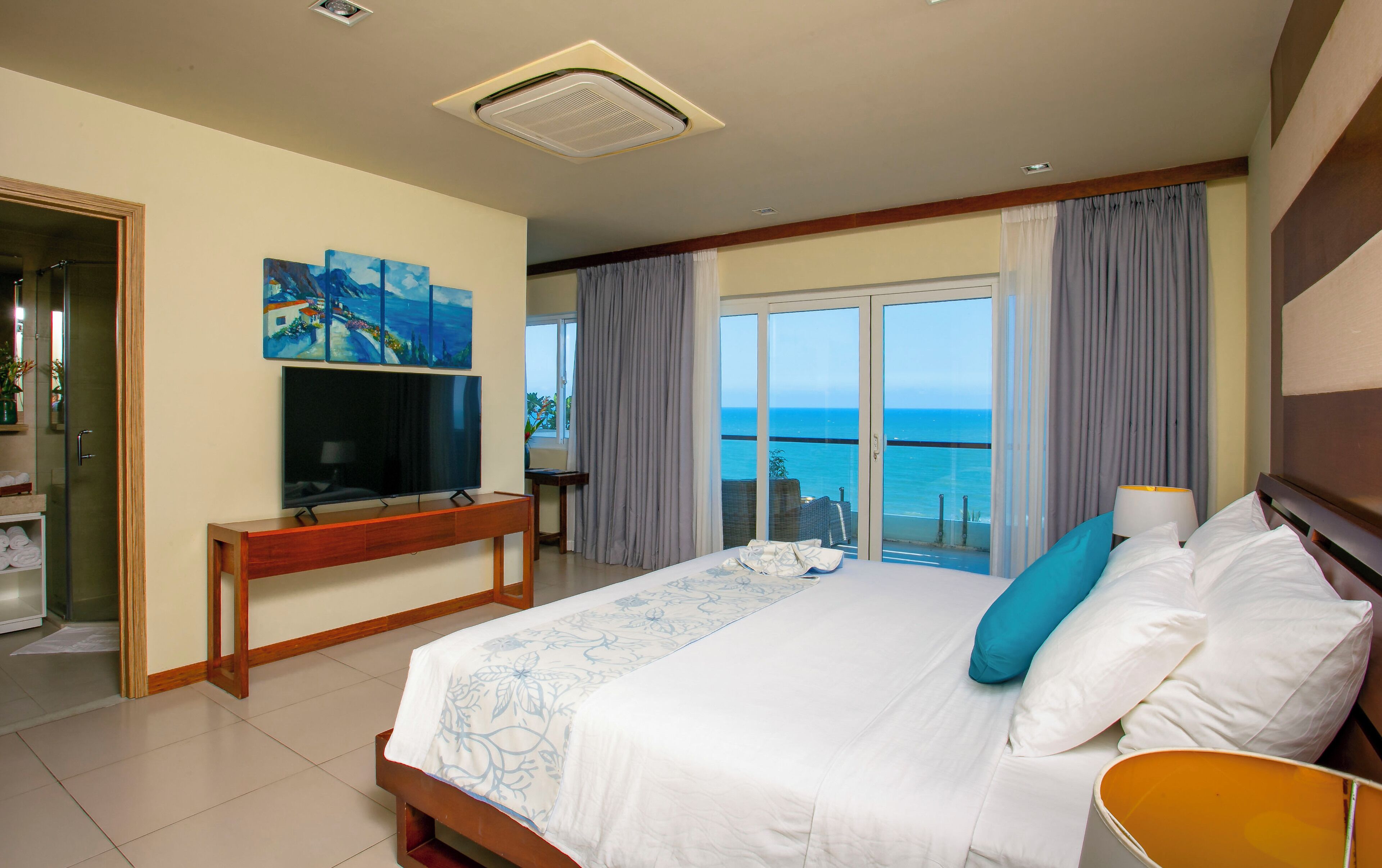 Camera d'albergo con un letto grande, televisione, balcone vista mare e zona doccia.