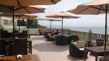 Une terrasse dotée de meubles en osier, de parasols beiges et offrant une vue sur la mer.