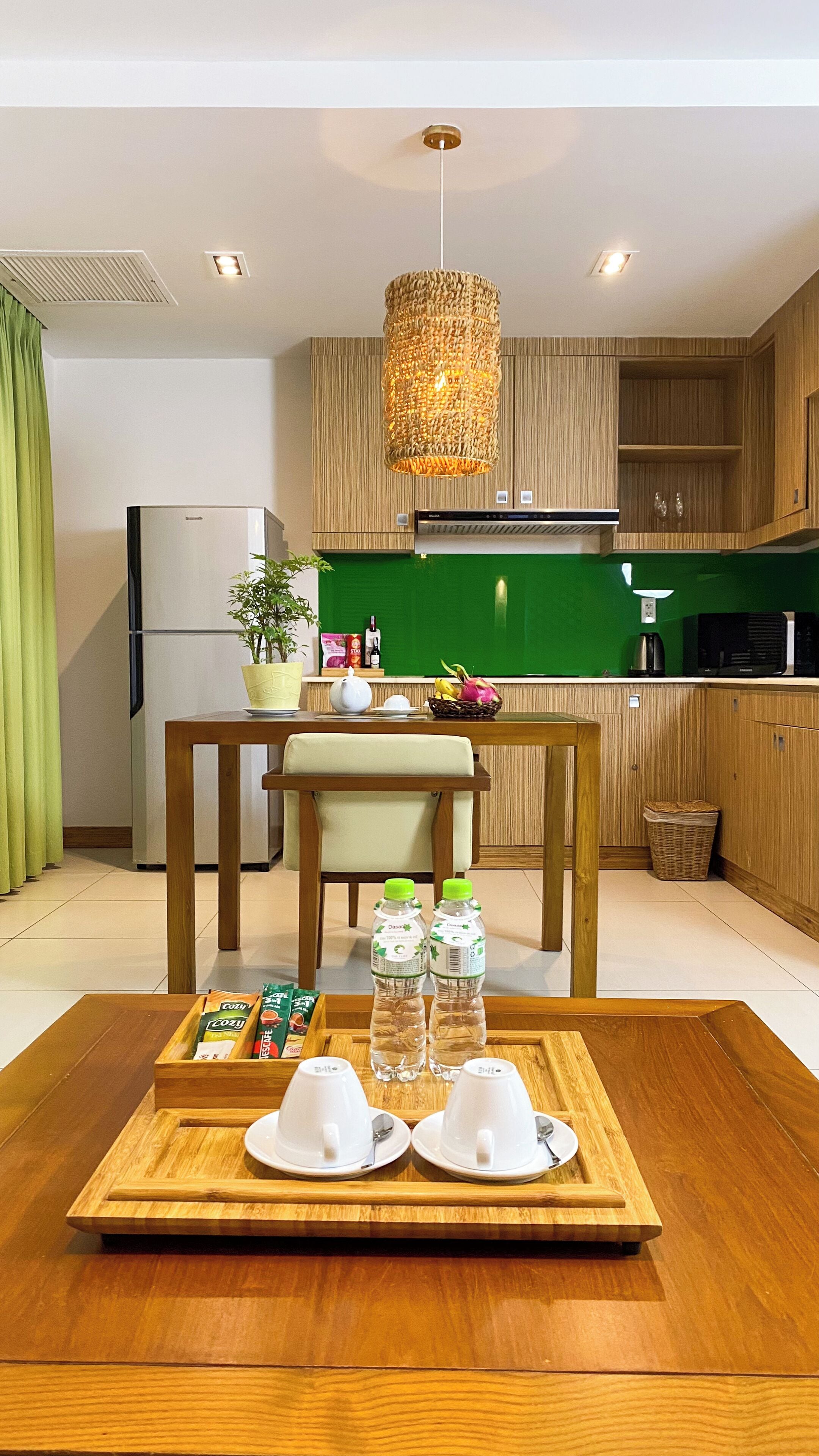 Een moderne keuken met houten kastjes, een eettafel met stoelen, een hanglamp en een dienblad met bekers en waterflessen.