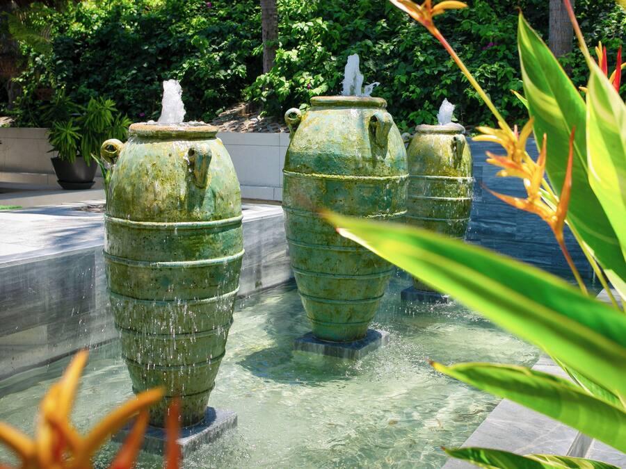 A series of large, green, weathered water fountains in a garden setting.