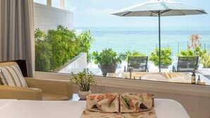 A hotel room with a bed, a window with a view of the ocean, a potted plant, and a table with chairs outside. - The Cliff Resort & Residences (Phu Thuy)