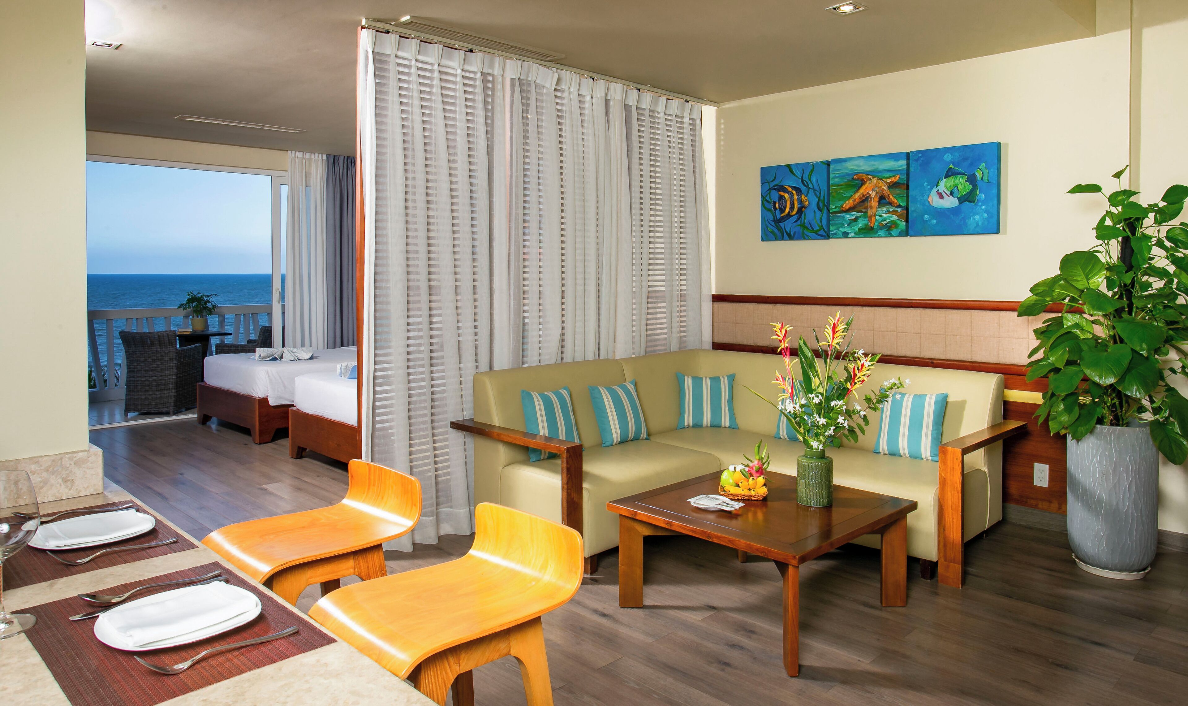 A hotel room with a balcony, a sofa, a dining table, and a view of the sea.
