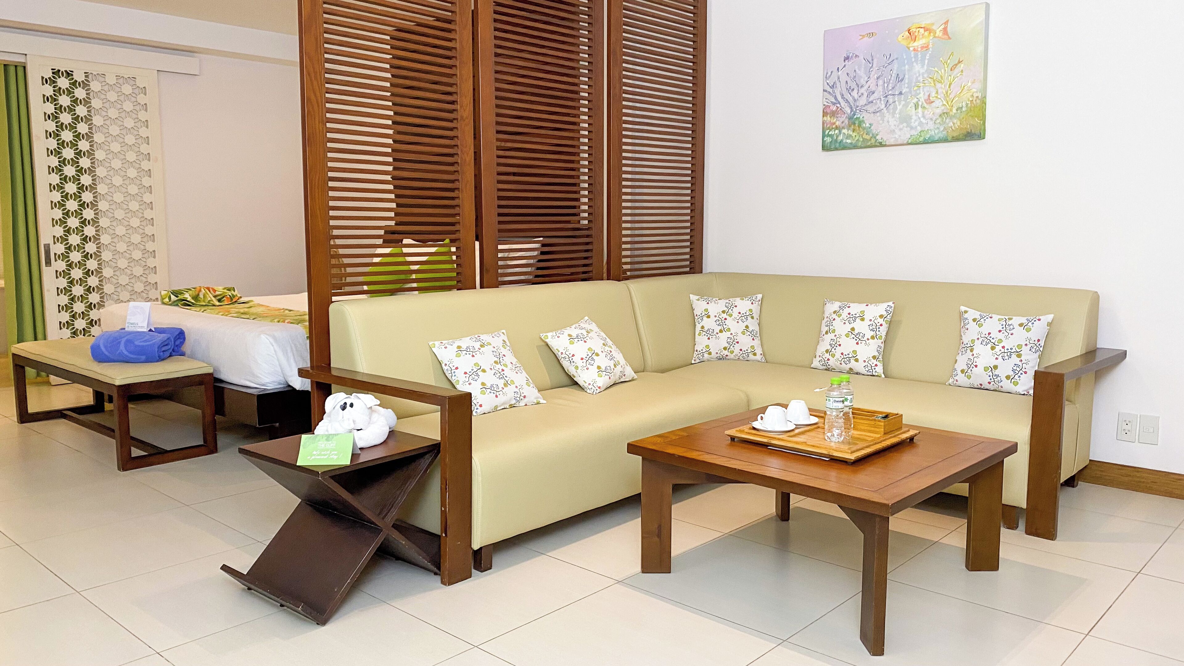 A hotel room with a sofa, two side tables, a bench, and a painting on the wall.