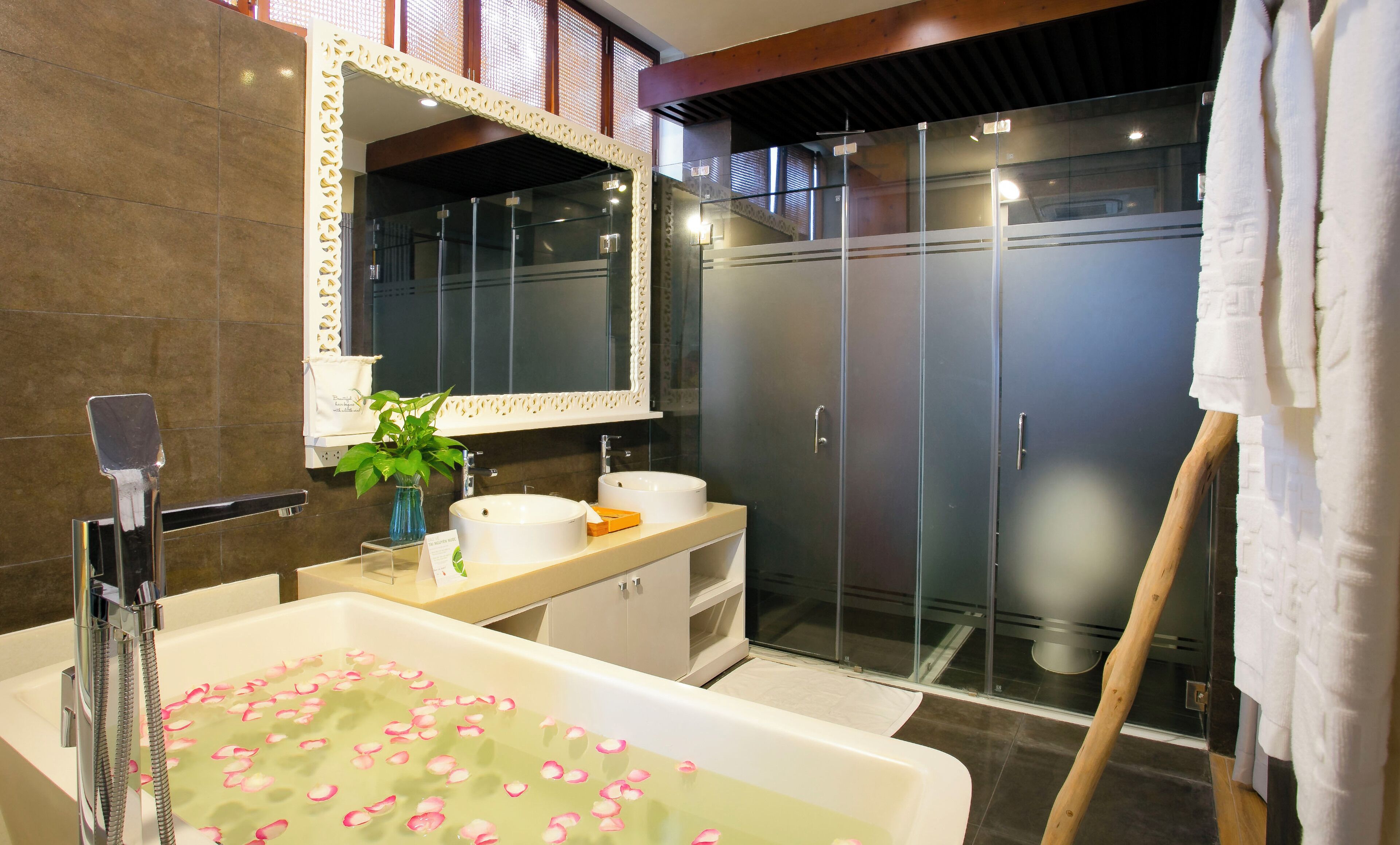 A modern bathroom with a bathtub filled with water and rose petals, a large mirror, and a glass shower enclosure.