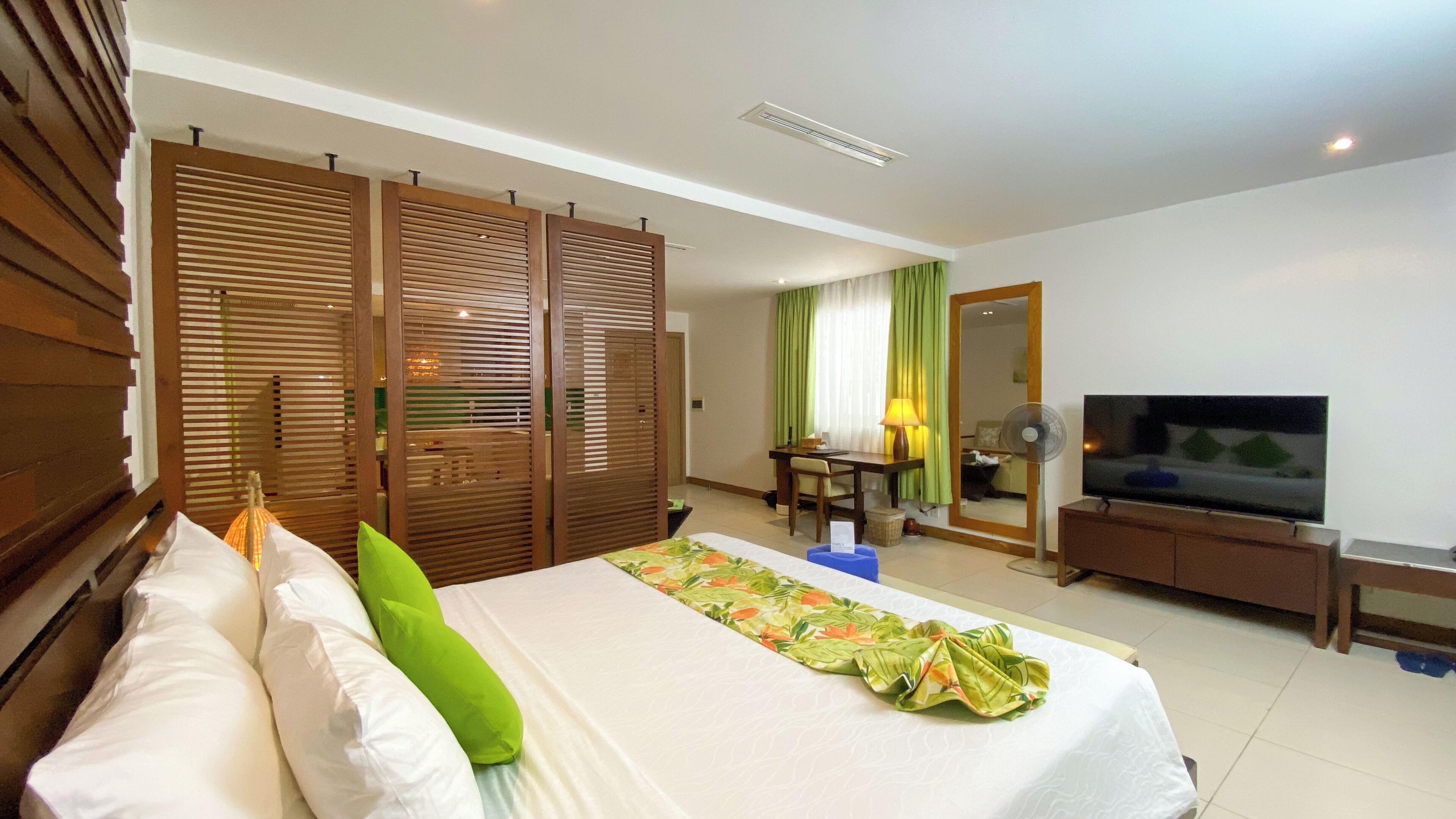 A hotel room with a bed, a desk, a chair, a TV, and a mirror.