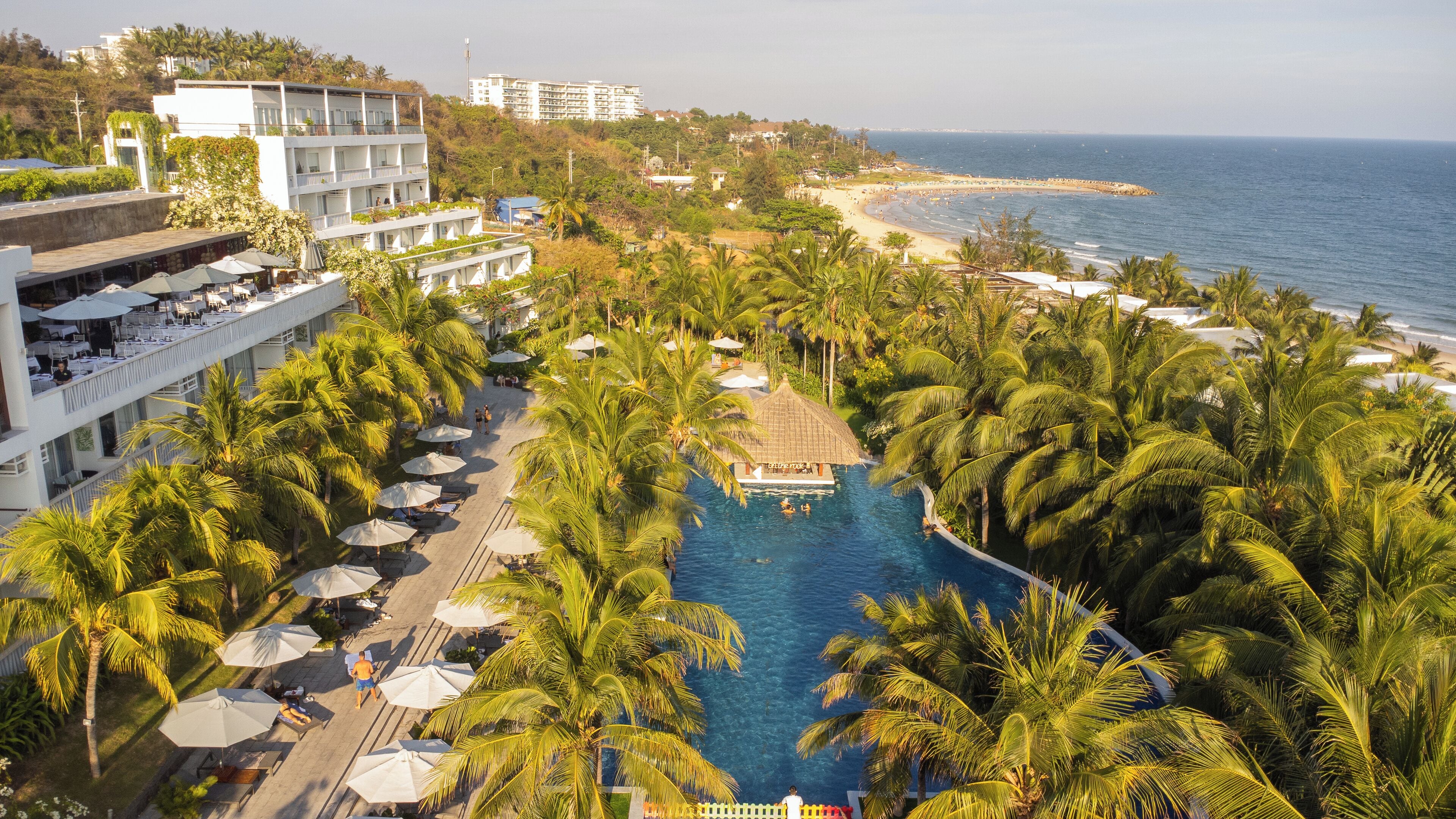 Un resort con piscina rodeada de palmeras, playa y vista al océano.