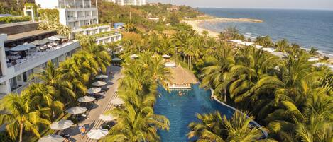 Un resort con piscina rodeada de palmeras, playa y vista al océano.
