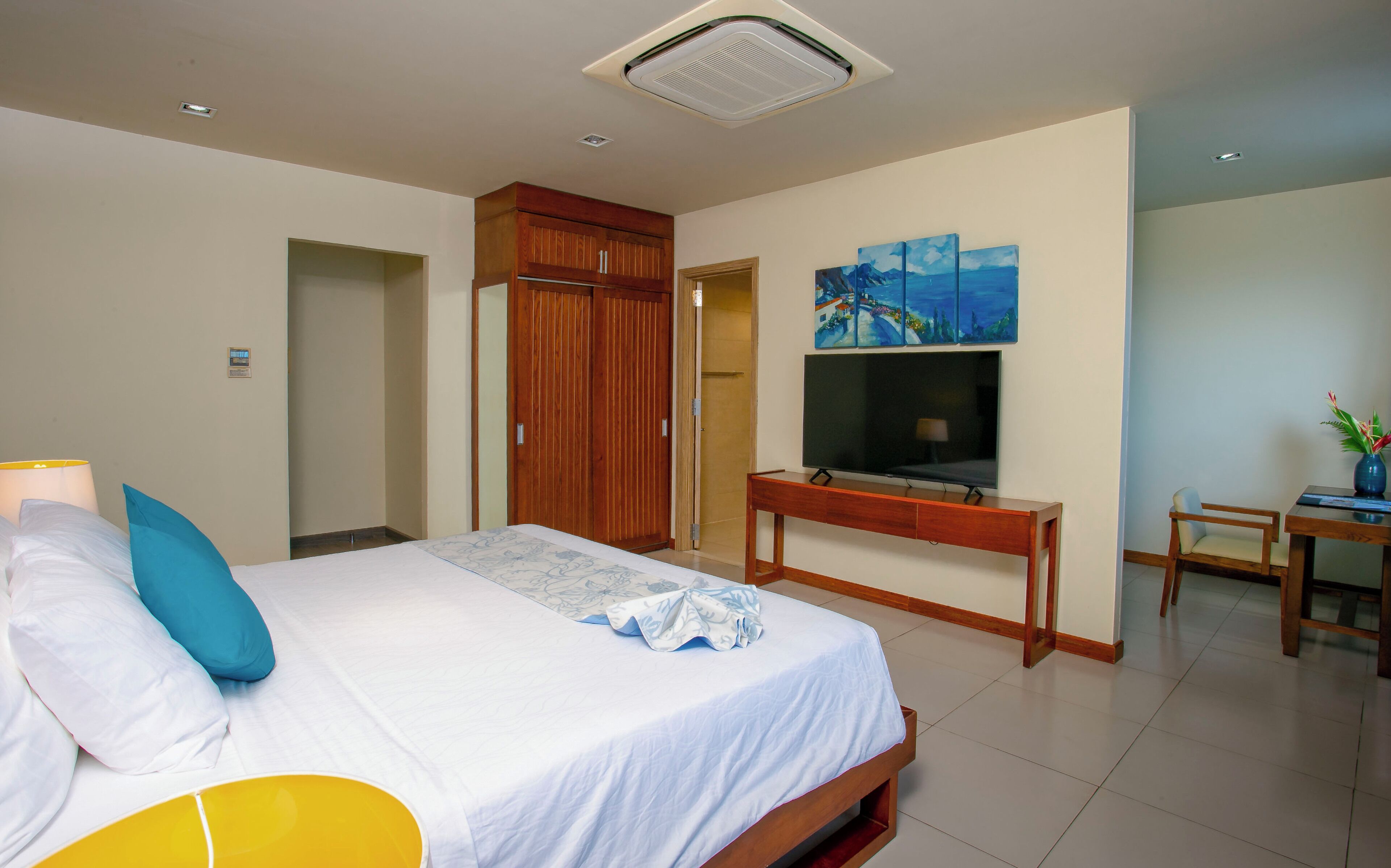 A hotel room with a bed, a desk, a TV, and a painting on the wall.