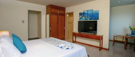A hotel room with a bed, a desk, a TV, and a painting on the wall.