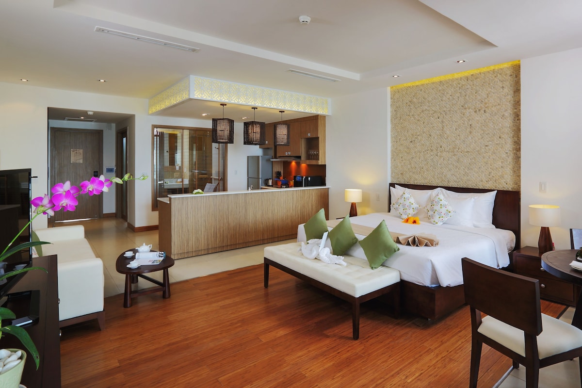 Una habitación de hotel con cama, zona de estar, escritorio, kitchenette y baño.