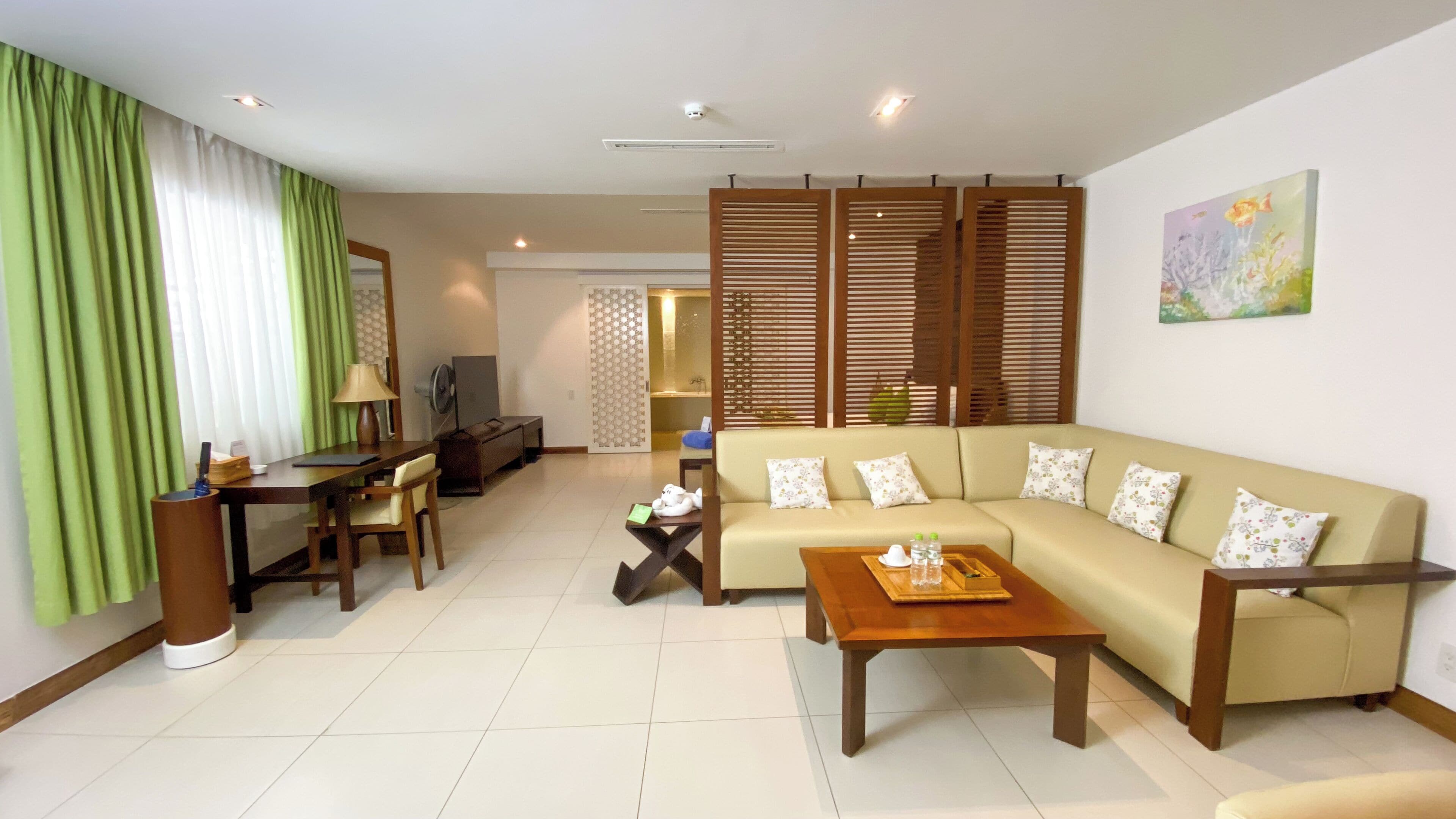 A living room with a sofa, coffee table, and a TV. There is a dining area with a table and chairs. The room has a green curtain and a wooden partition.