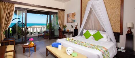 Ein Hotelzimmer mit Bett, einer Bank, einem Schreibtisch, einem Stuhl, einem Nachttisch und Blick auf den Strand.