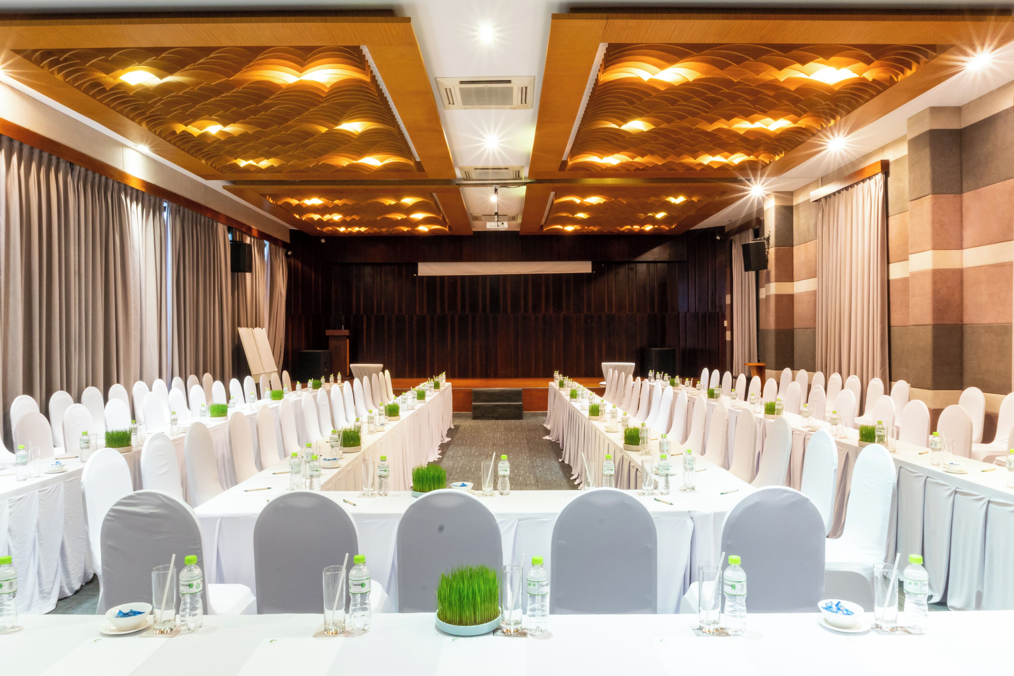 A conference room with long tables, white chairs, and a stage at the front.