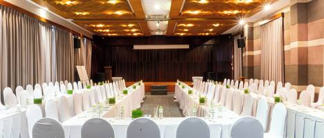 A conference room with long tables, white chairs, and a stage at the front.