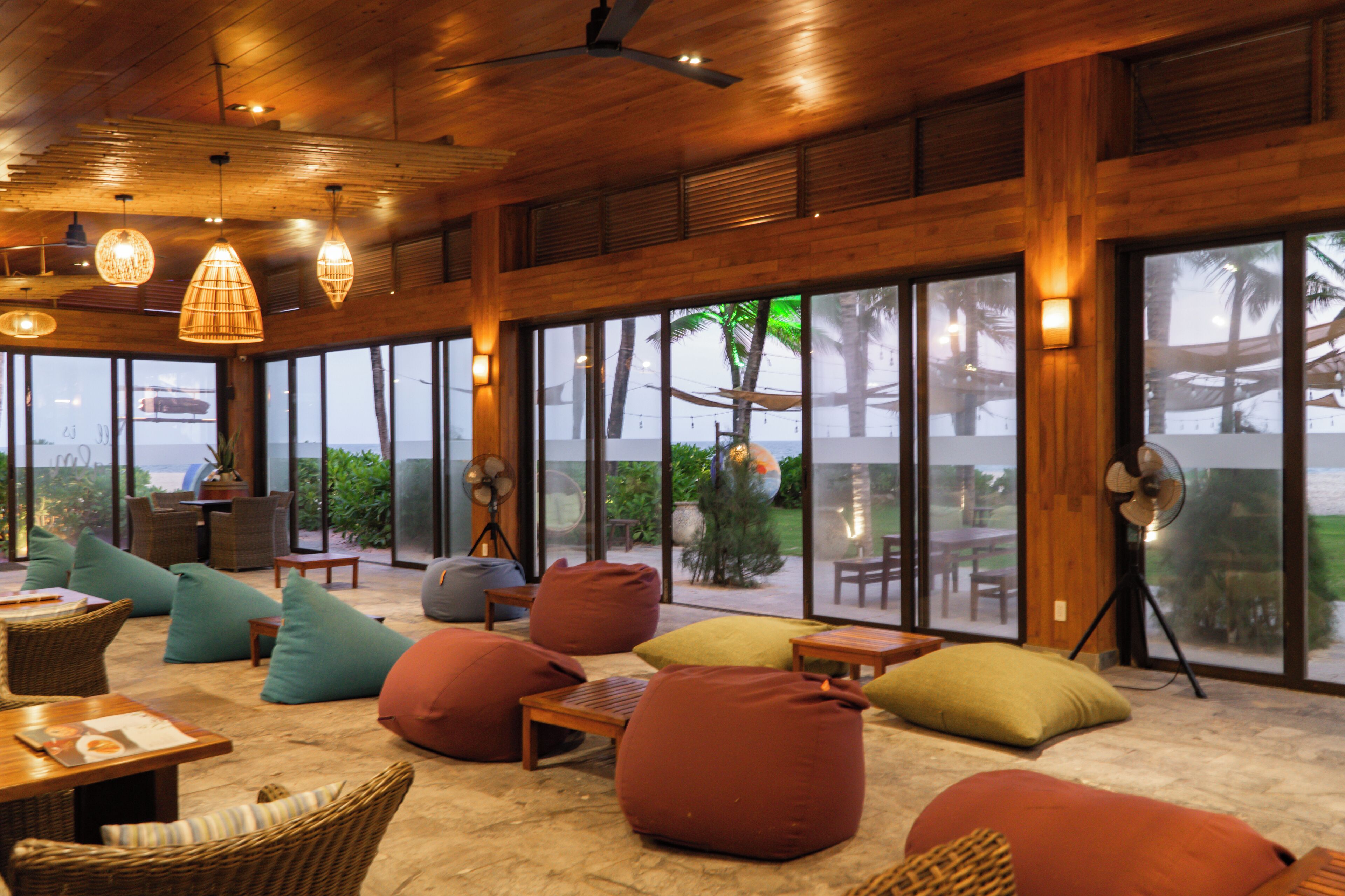 A spacious indoor area with large windows, wooden furniture, and bean bags.