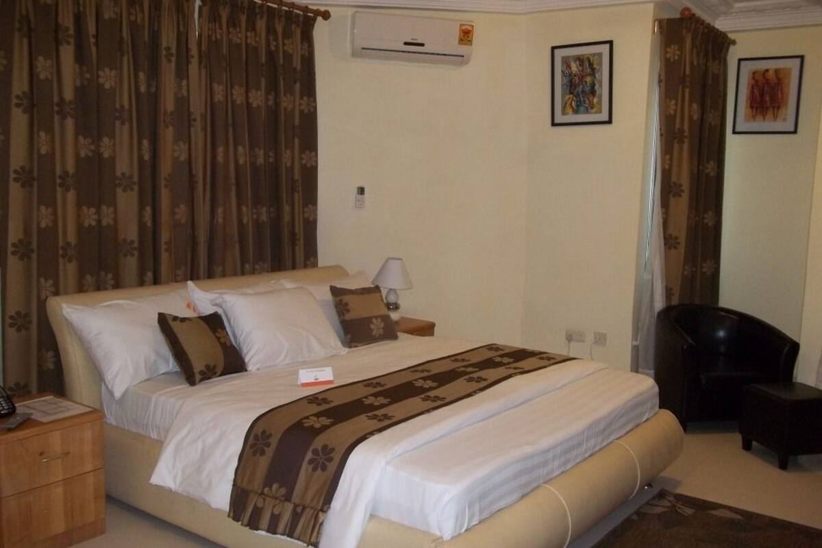 Una habitación de hotel con cama, mesita de noche, una silla y un equipo de aire acondicionado.