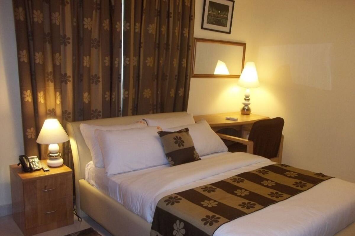 Habitación de hotel con cama, lámparas de noche, mesita con teléfono y ventana con cortinas.