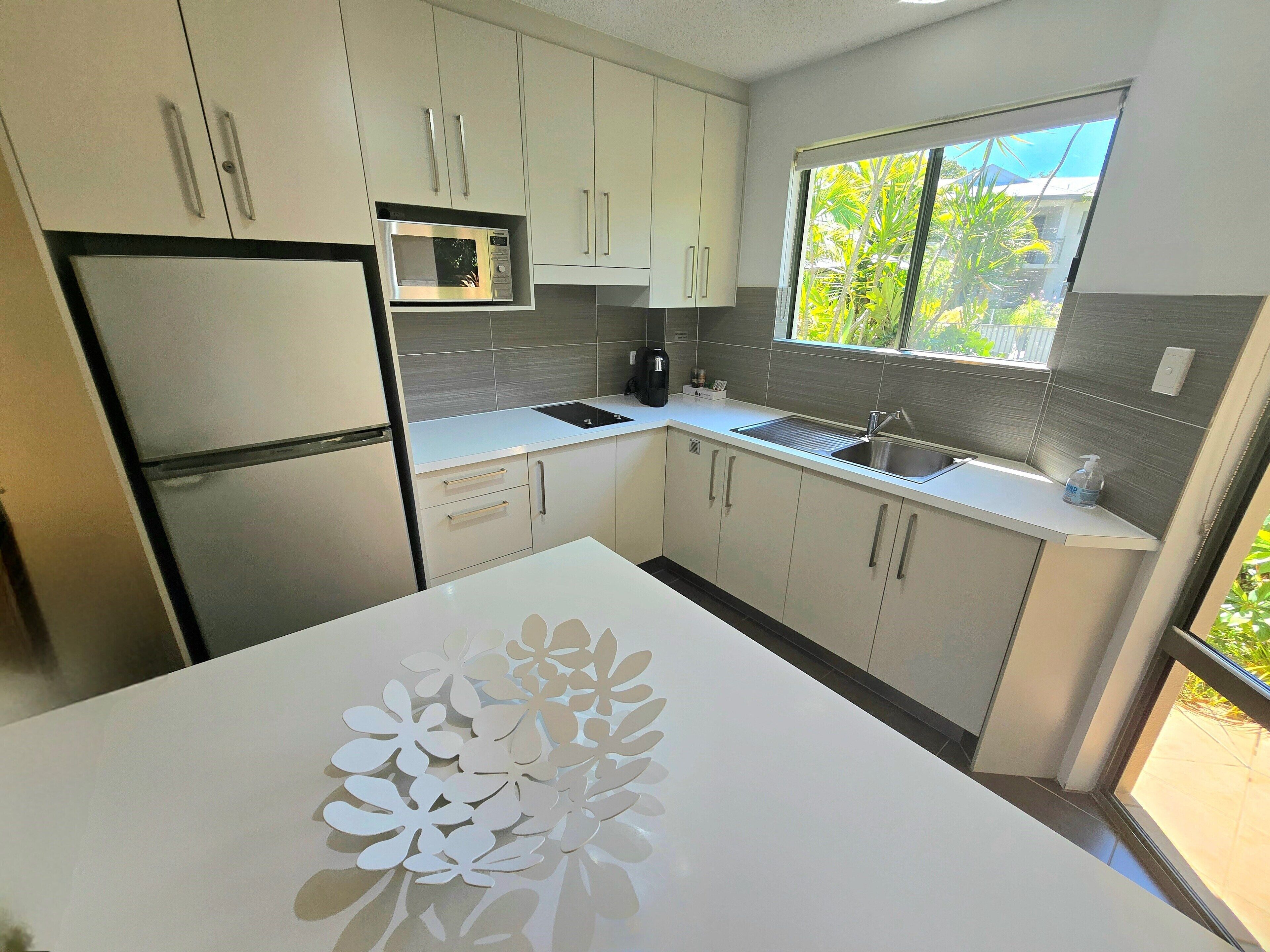 A modern kitchen with white cabinets, a stainless steel refrigerator, a microwave, and a sink.