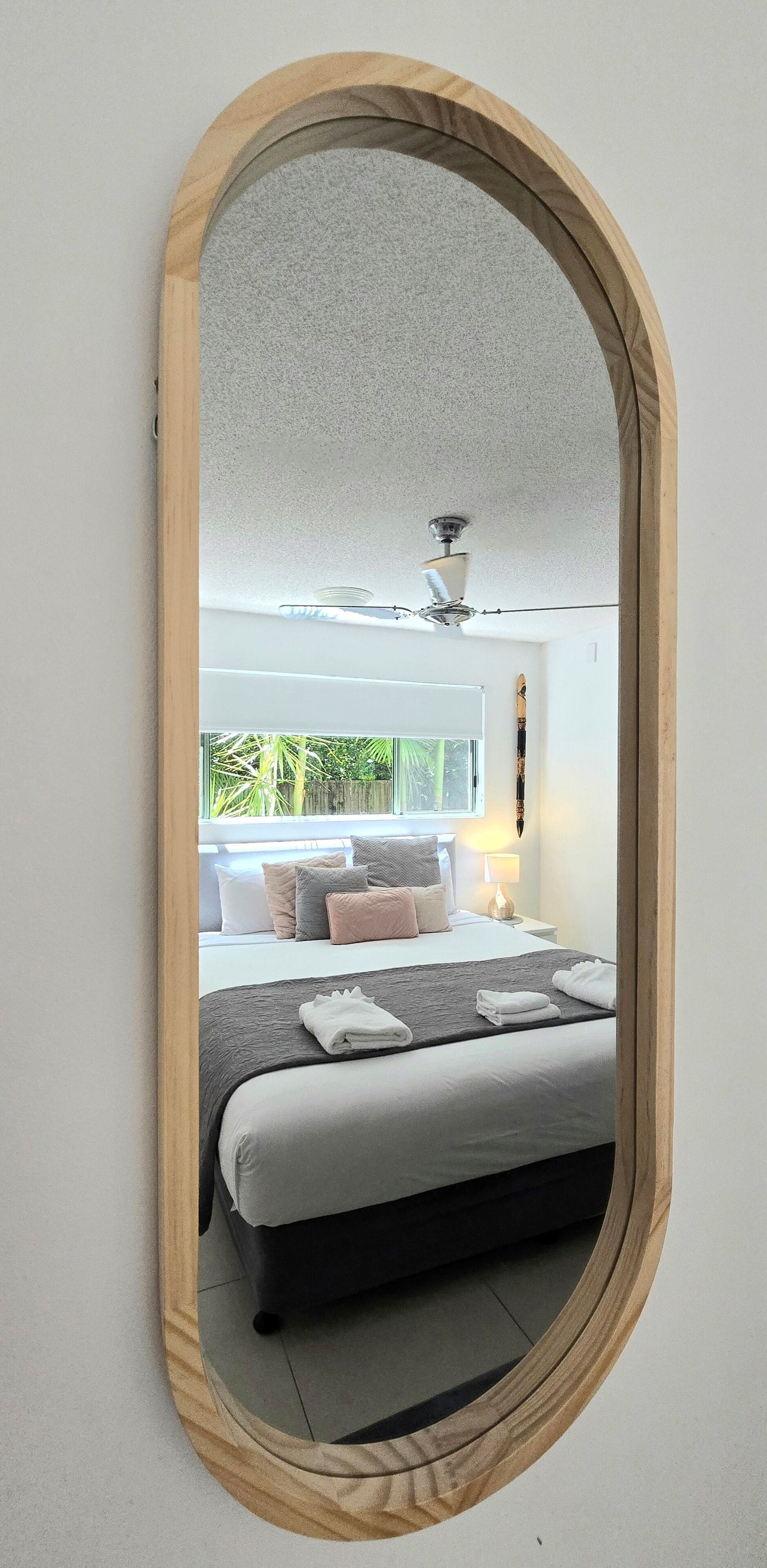 Een slaapkamer met een bed, kussens, een nachtkastje, een lamp en een plafondventilator.