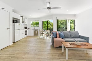 Een moderne keuken met witte kasten, een eethoek met tafel en stoelen, en een grijze bank met een houten salontafel.