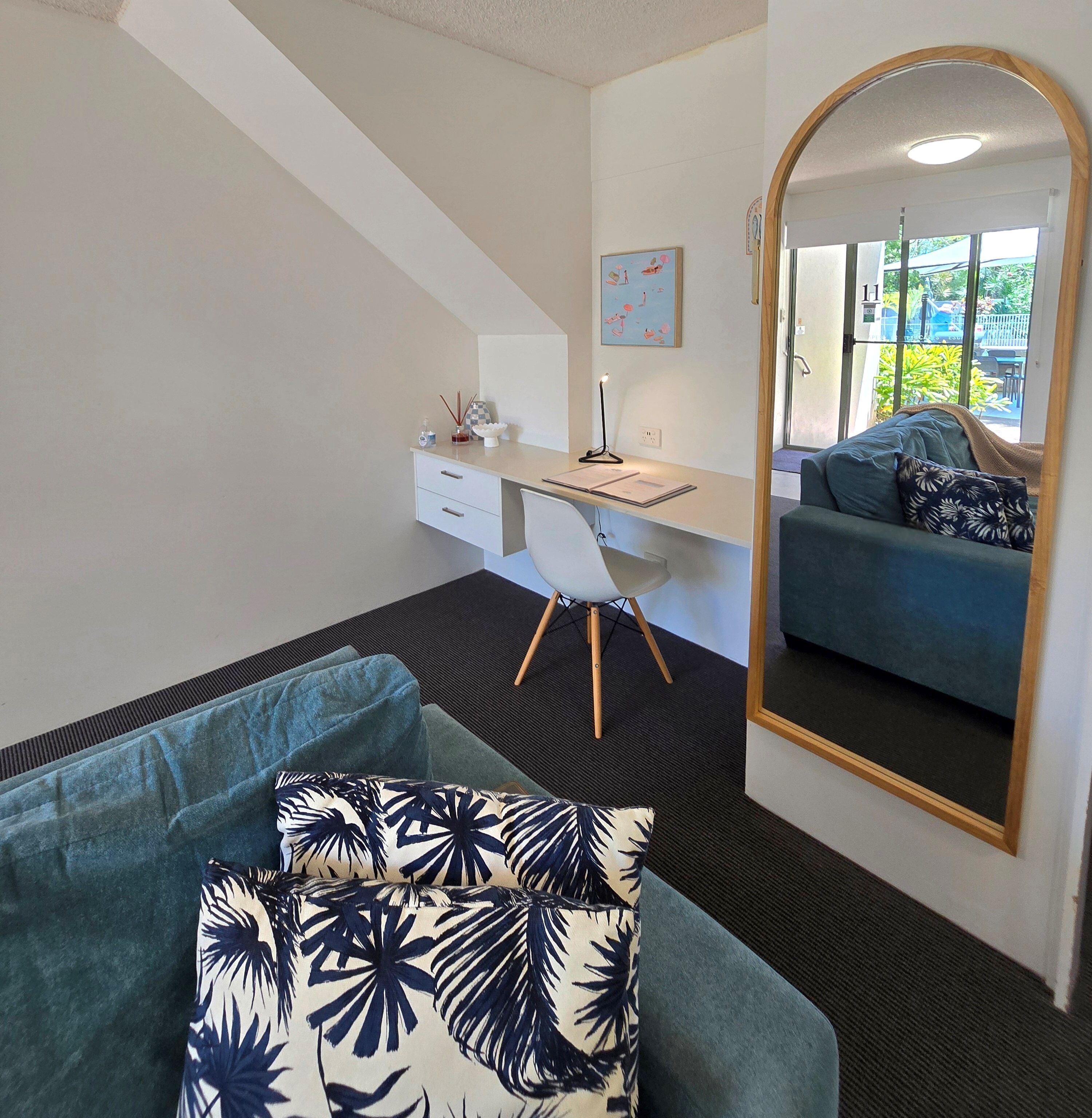 Un dormitorio moderno con escritorio, un espejo grande, un sofá y vistas al exterior.