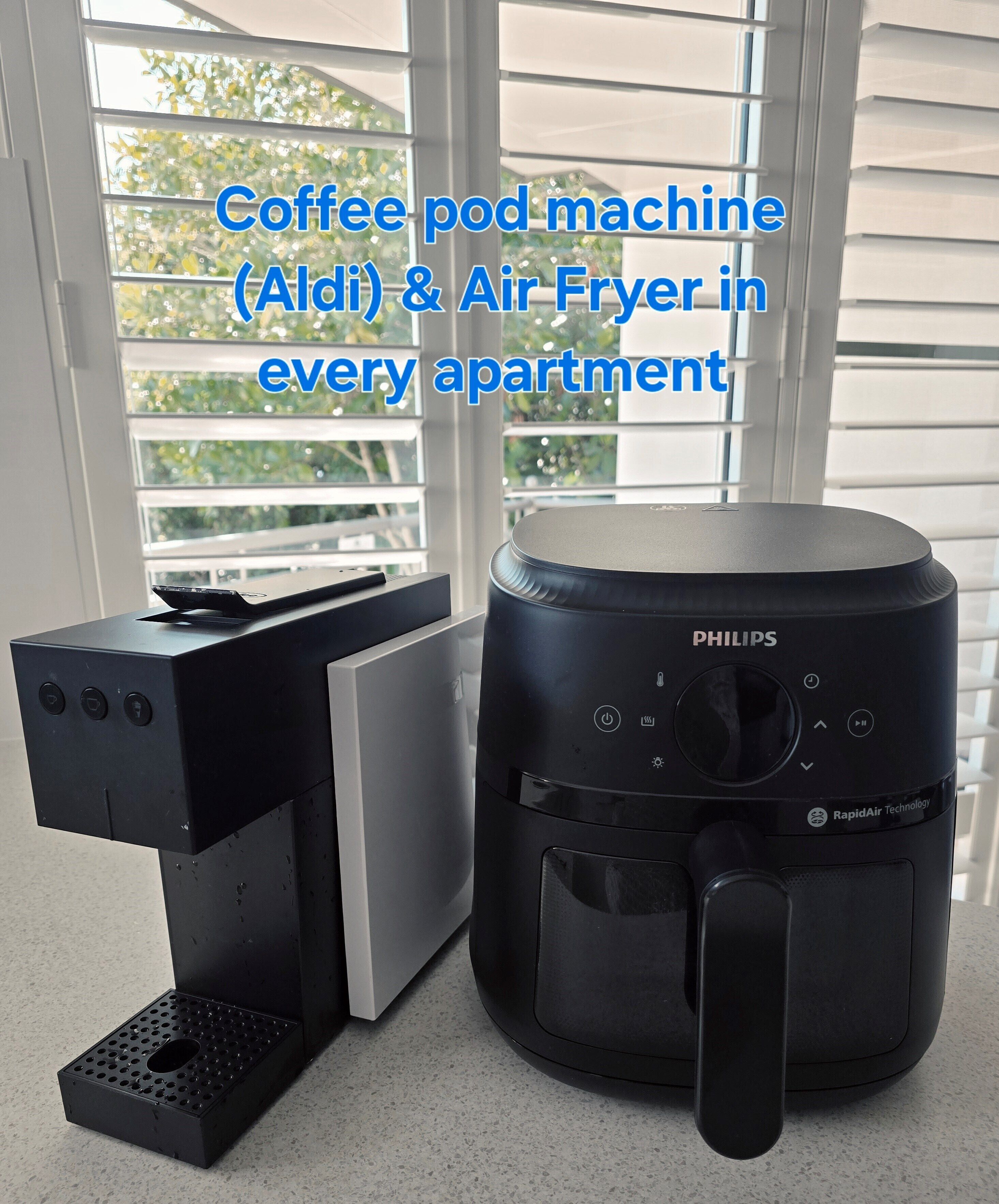 Una máquina para cápsulas de café y una freidora de aire sobre una encimera cerca de una ventana con persianas.