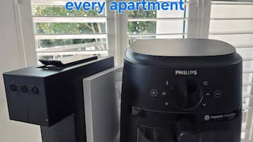Una máquina para cápsulas de café y una freidora de aire sobre una encimera cerca de una ventana con persianas.
