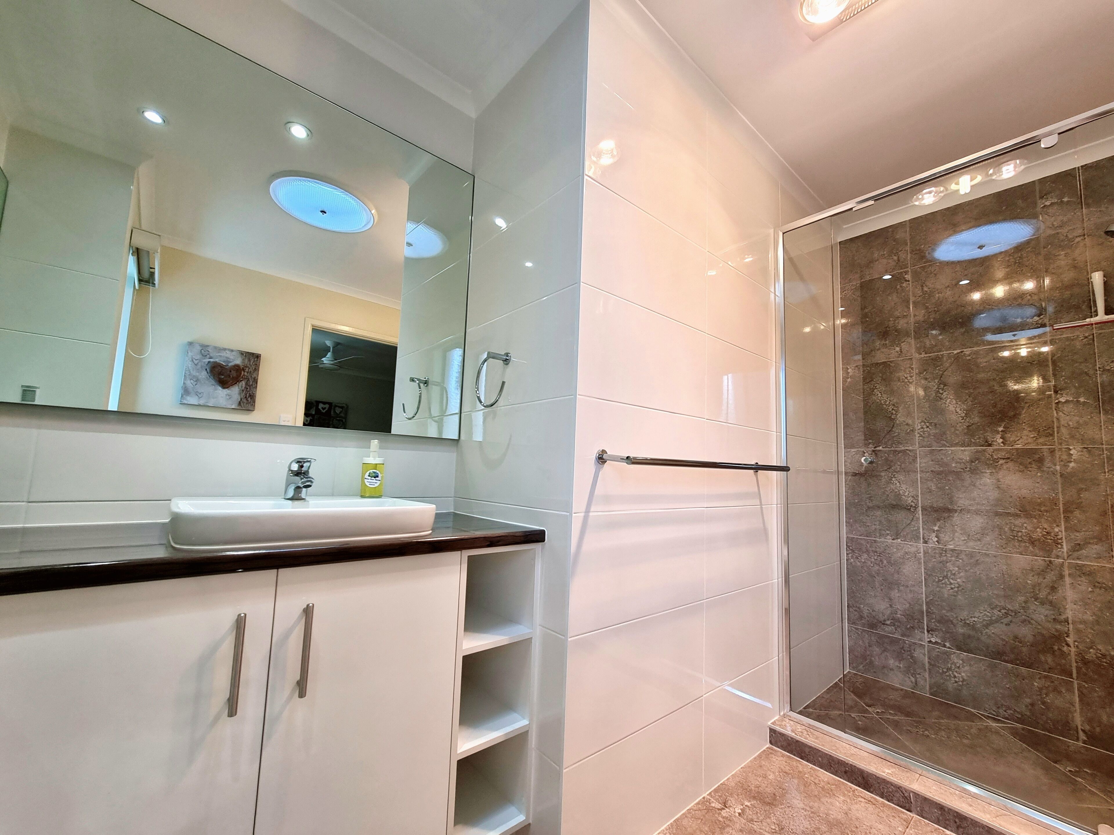 Ein modernes Badezimmer mit einem weißen Waschbecken, einer Duschkabine aus Glas und einem großen Spiegel.