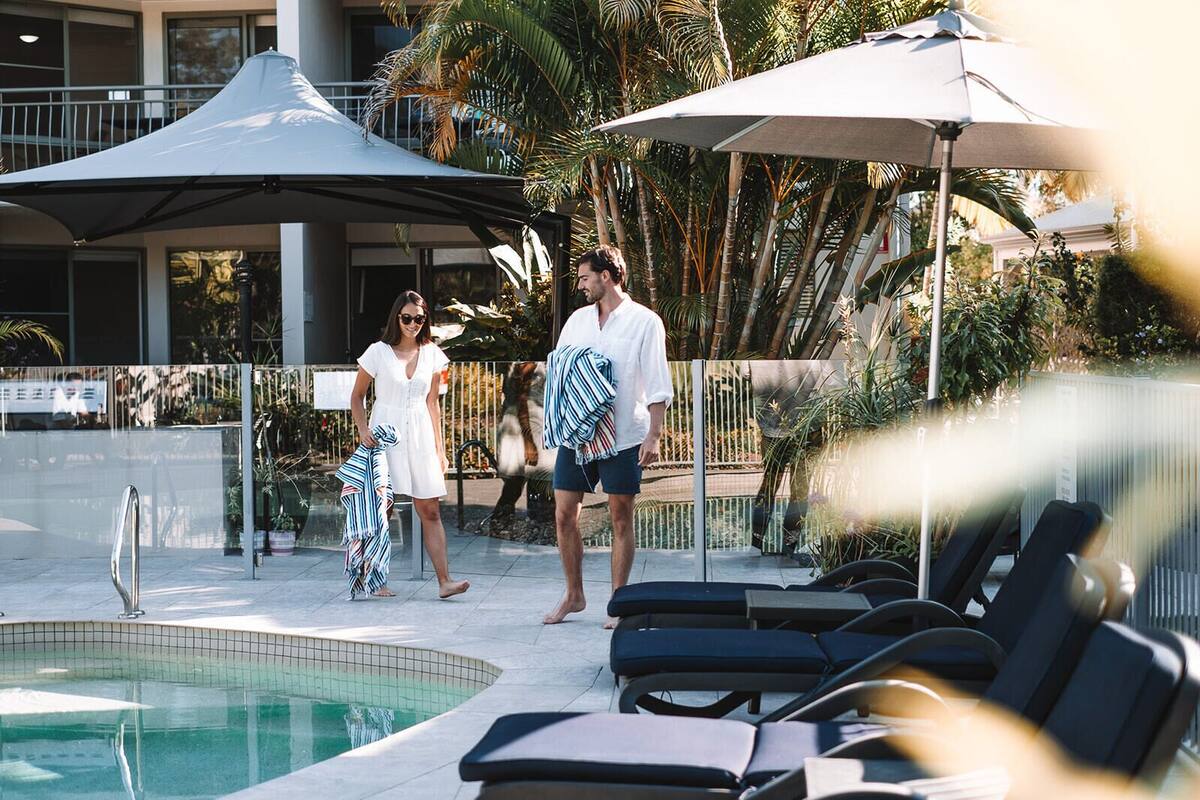 Un espace aménagé au bord de la piscine, avec des chaises longues, des parasols et une piscine.