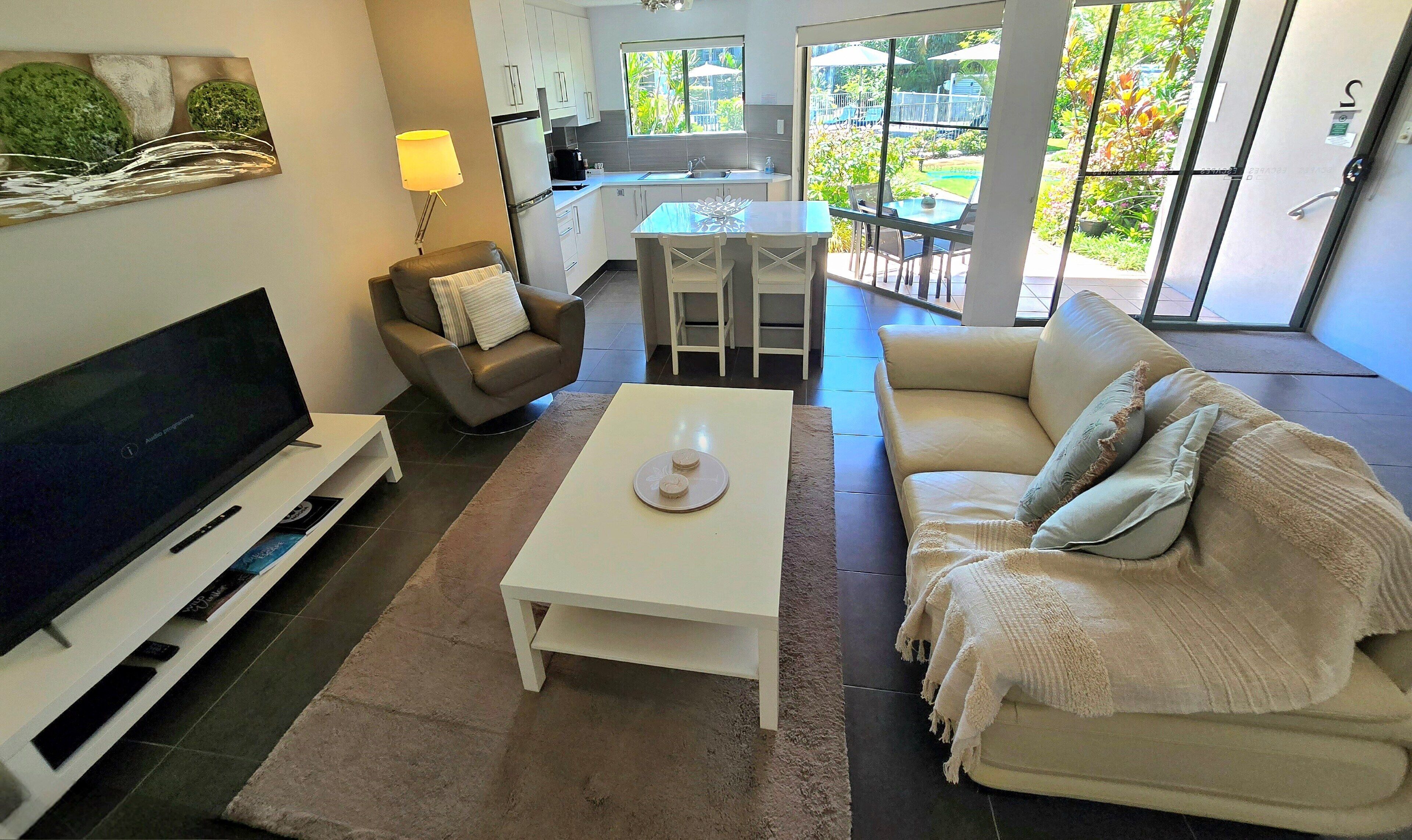 Een moderne woonkamer met een flatscreen televisie, een bank, een salontafel en een eethoek met stoelen.