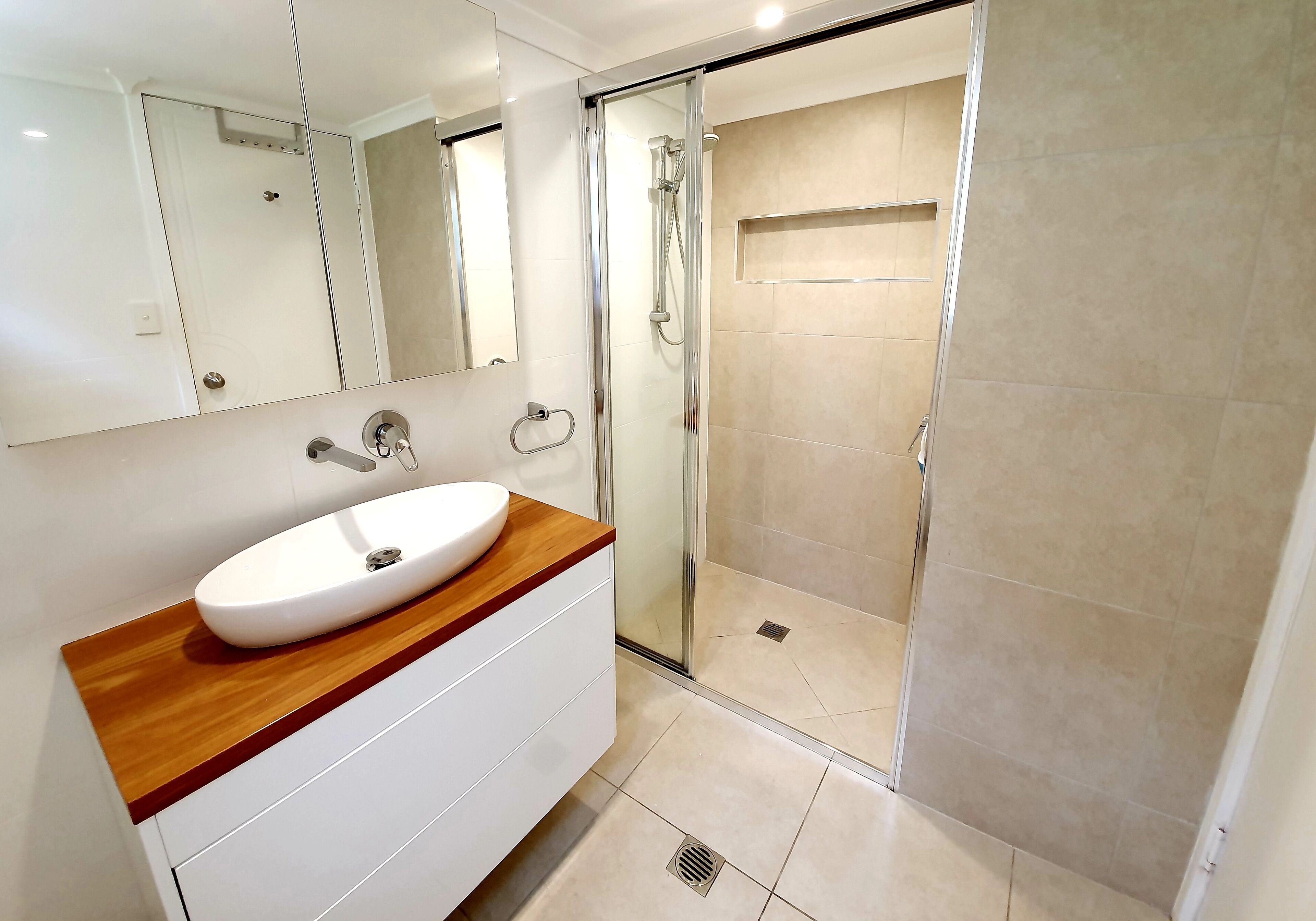 Un baño moderno con un lavabo blanco, encimera de madera y zona de ducha con mampara de vidrio.