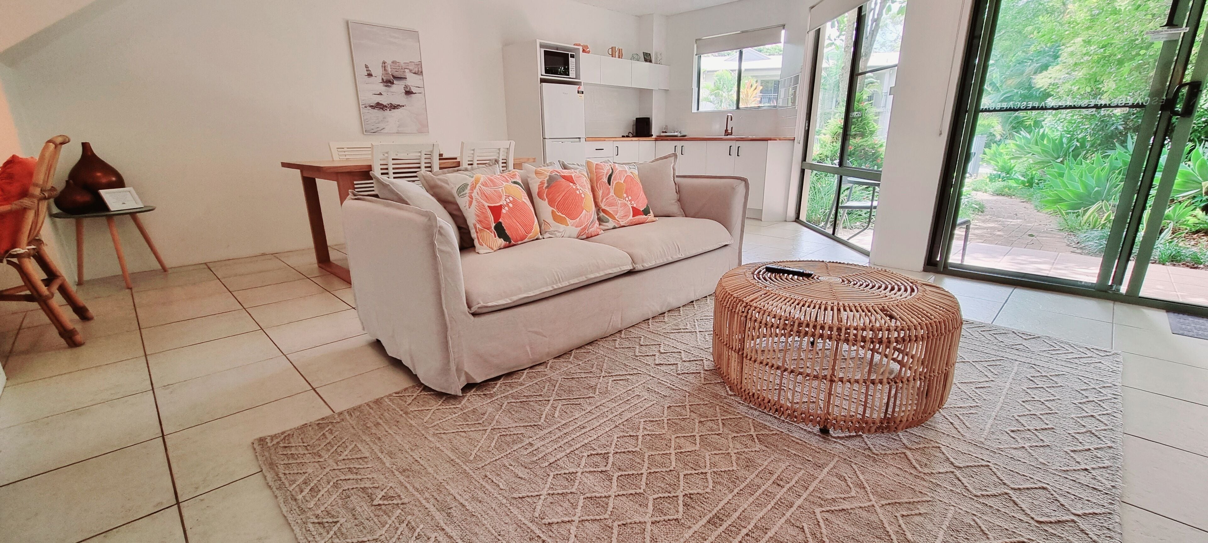 A modern living room with a sofa, a round wicker ottoman, and a patterned rug.