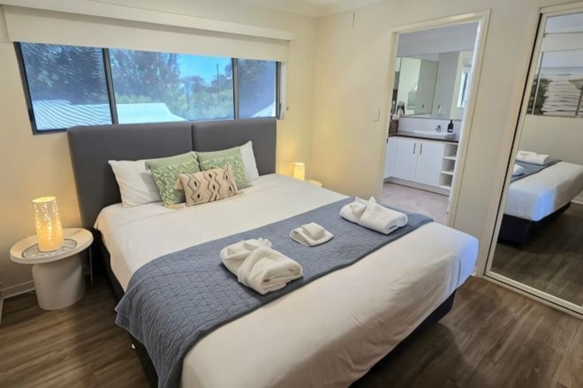 Habitación de hotel con una cama grande, lámparas de noche, un espejo y vistas al exterior.