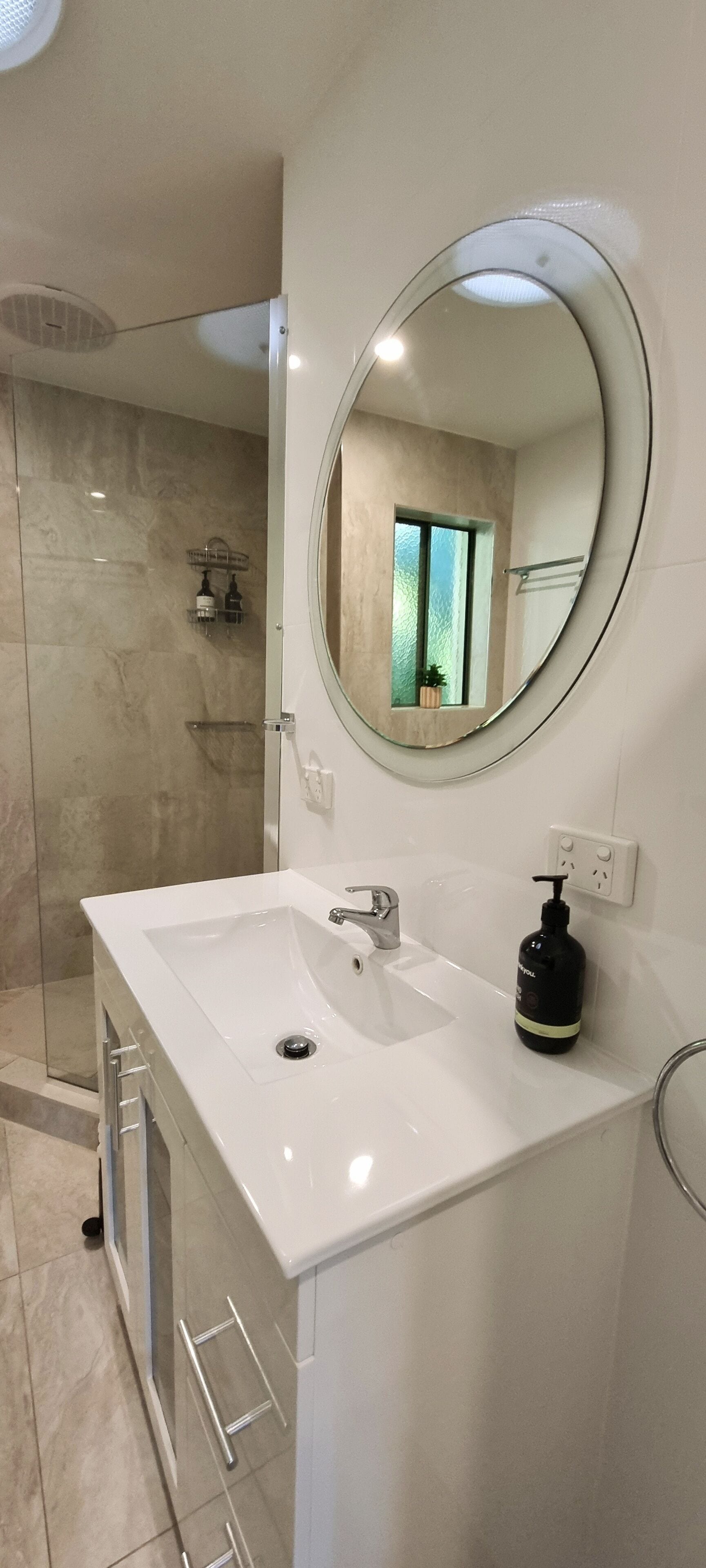Un baño con lavamanos blanco, un espejo redondo y zona de ducha.