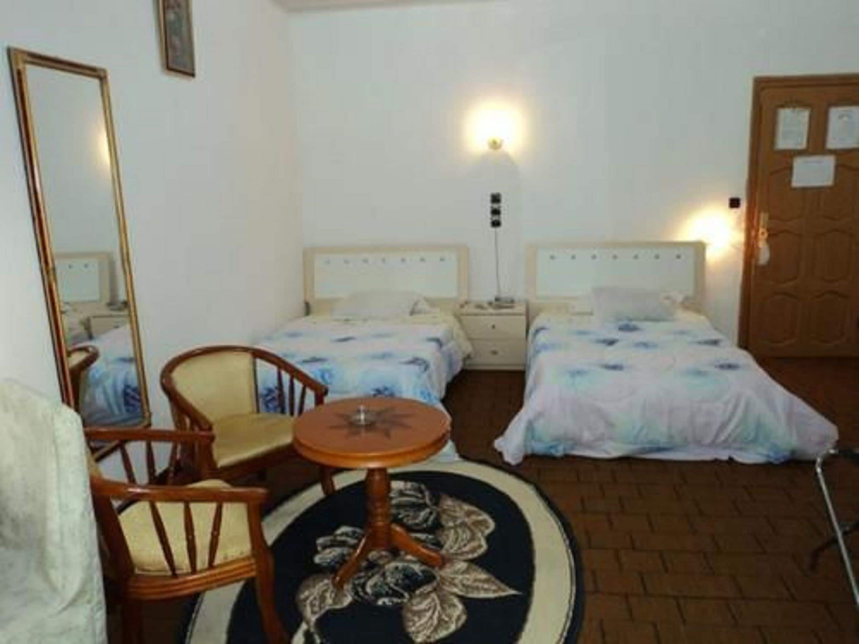 Habitación de hotel con dos camas, una mesa redonda, una silla, un espejo y una puerta con un aviso.