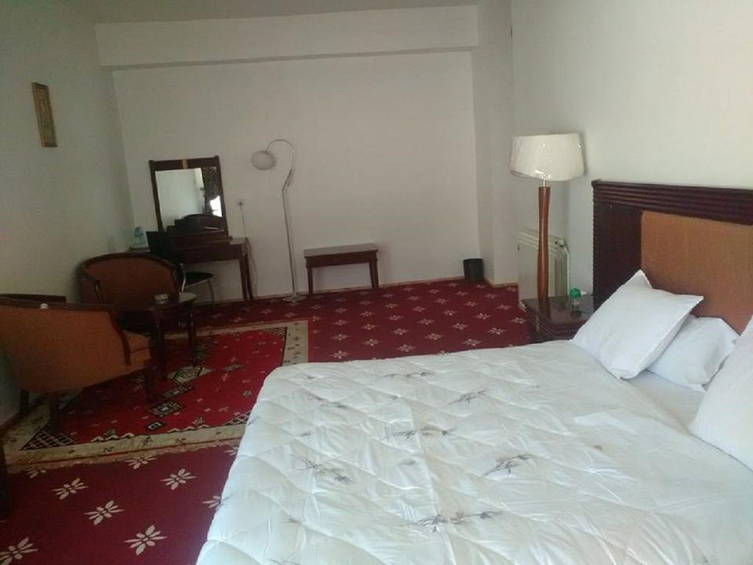 A hotel room with a bed, a desk, a chair, a lamp, and a carpeted floor.