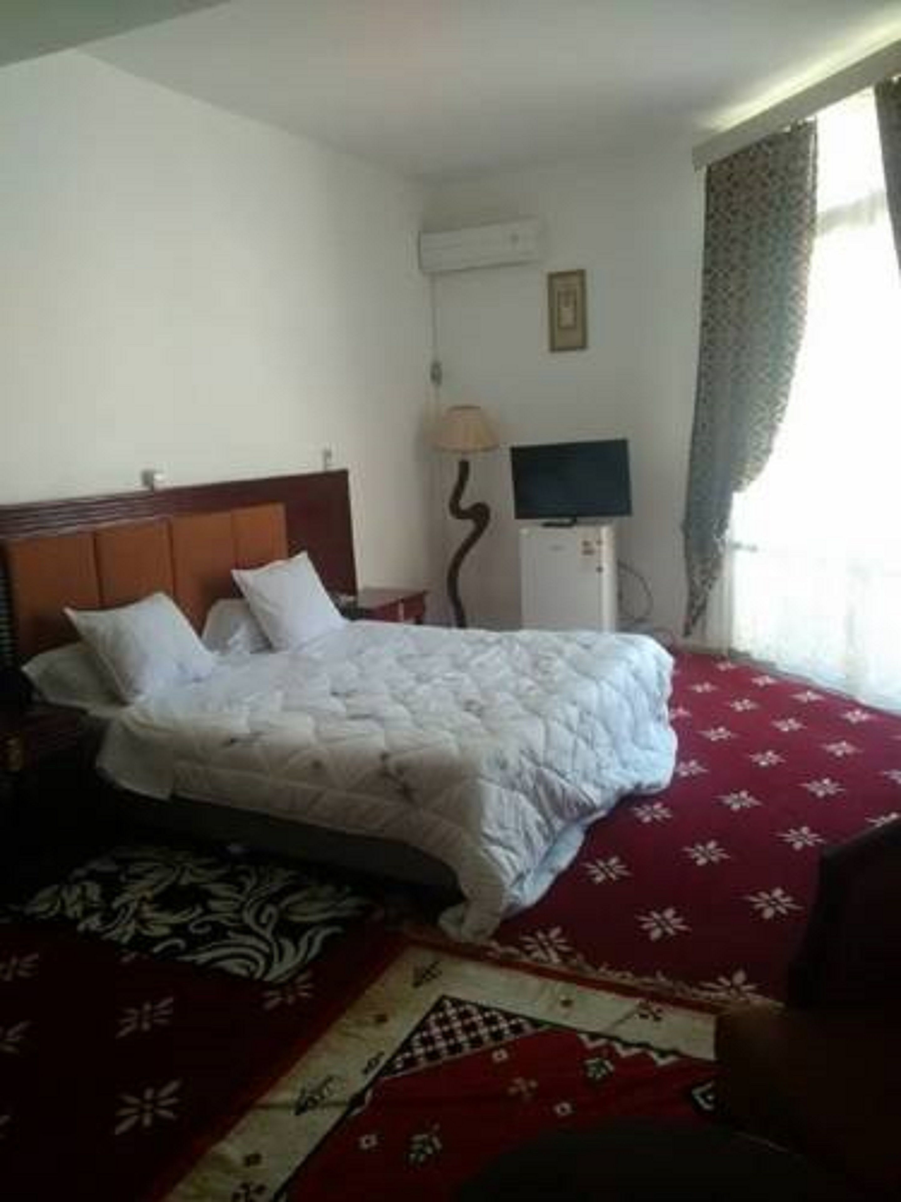 Une chambre d’hôtel équipée d’un lit, d’une télévision, d’un climatiseur et d’une fenêtre avec des rideaux.