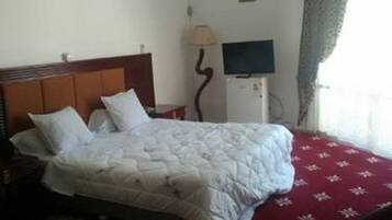 A hotel room with a bed, a TV, an air conditioning unit, and a window with curtains.