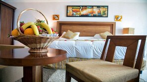 Una habitación de hotel con una cama, una cesta de mimbre con fruta sobre una mesa y una silla.
