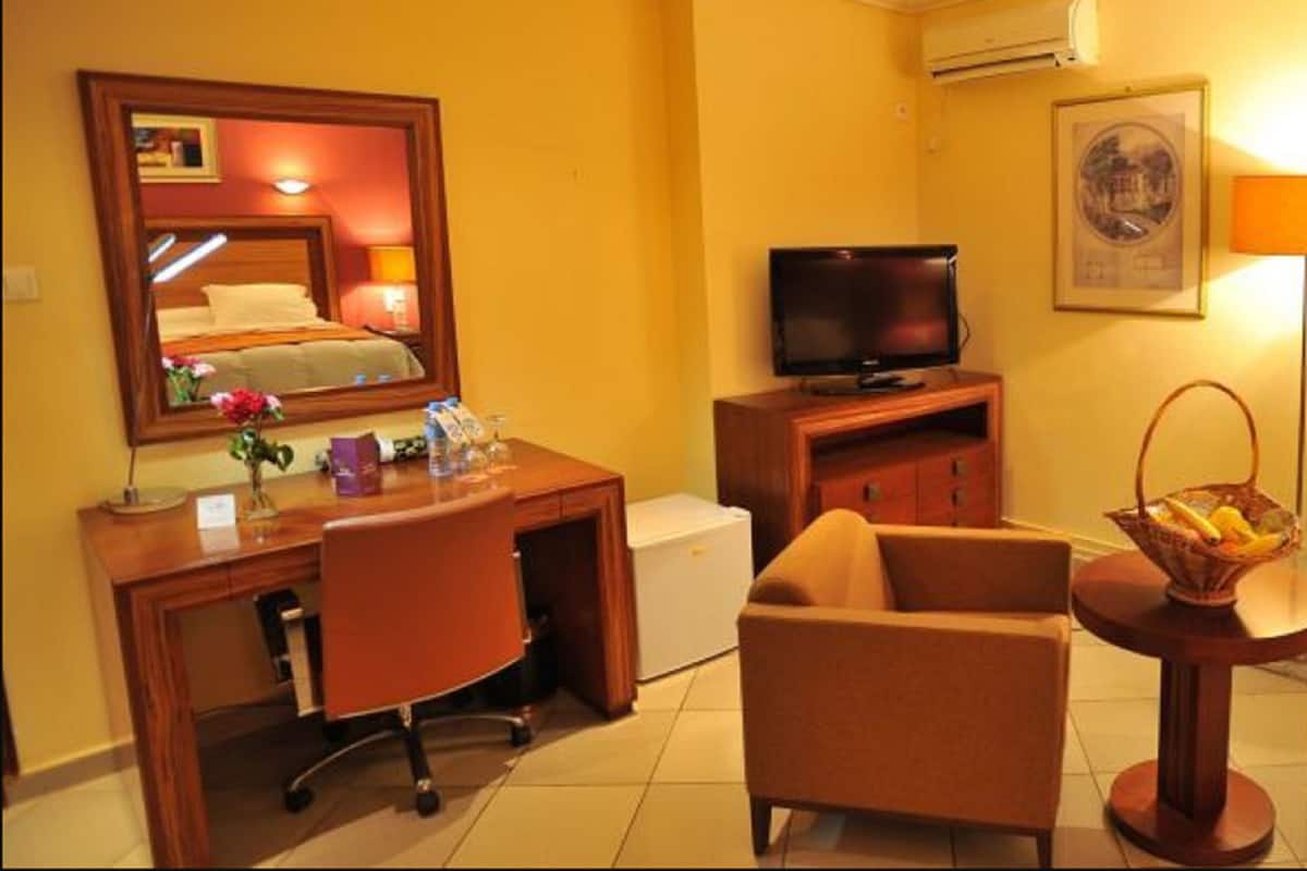 A hotel room with a desk, chair, television, and a small table with a basket.