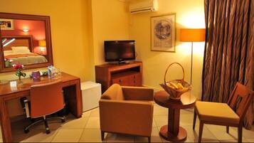Habitación de hotel con escritorio, silla, televisión y una mesita con una cesta.