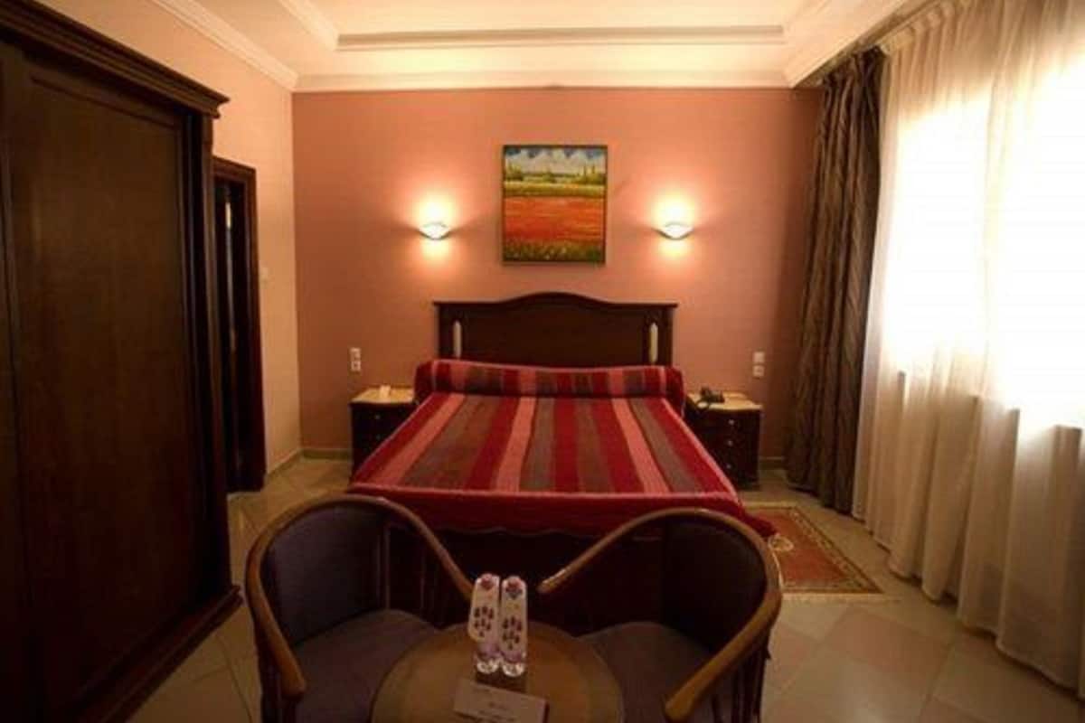 A hotel room with a large bed, two bedside tables, a chair, a desk with a telephone, and a painting on the wall.