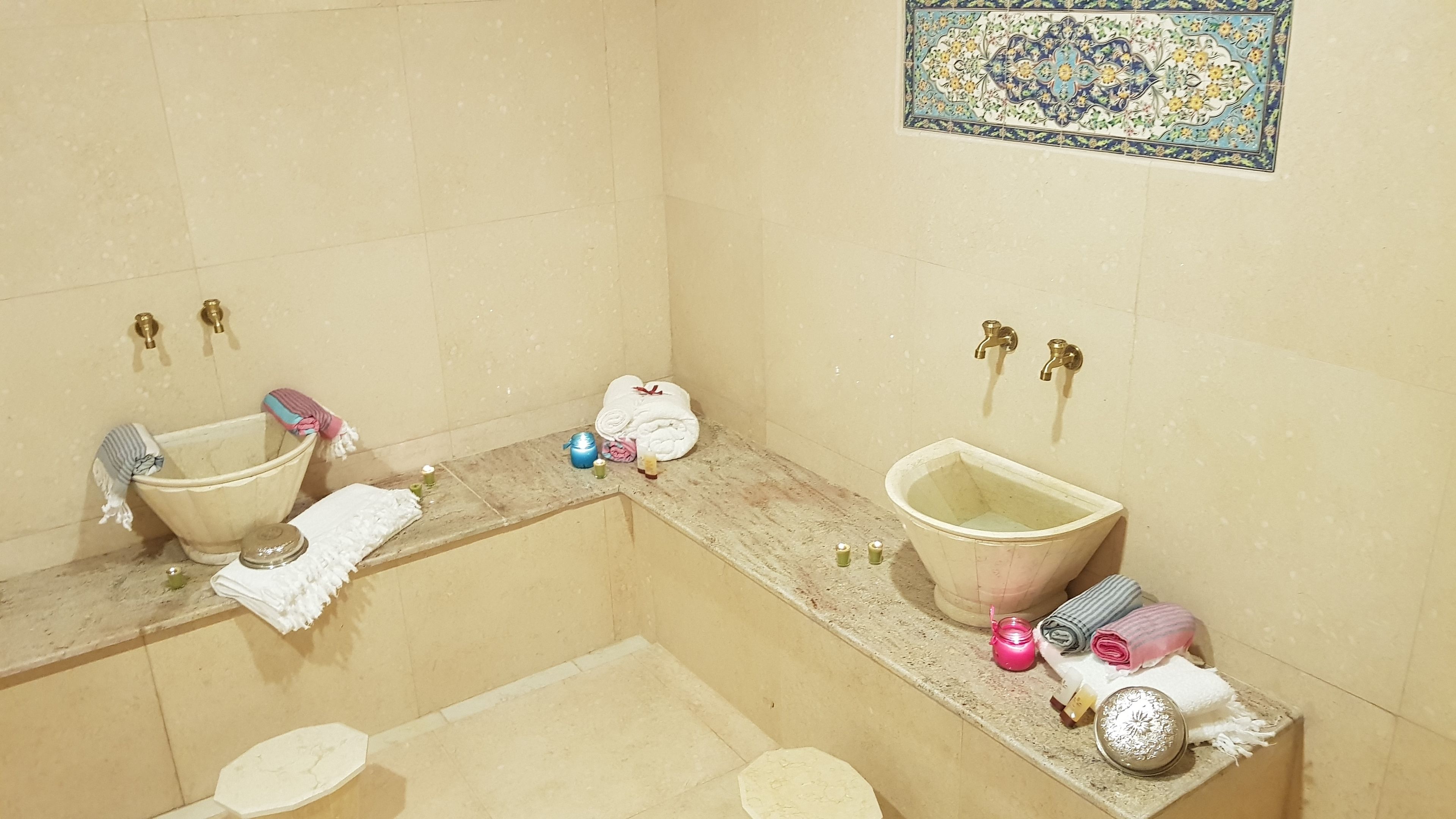 Baño con dos lavamanos, bañera y ducha. Hay toallas, dispensador de jabón y un azulejo decorativo en la pared.