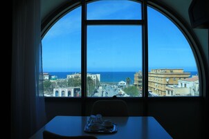 A room with a large arched window overlooking a cityscape and the sea.