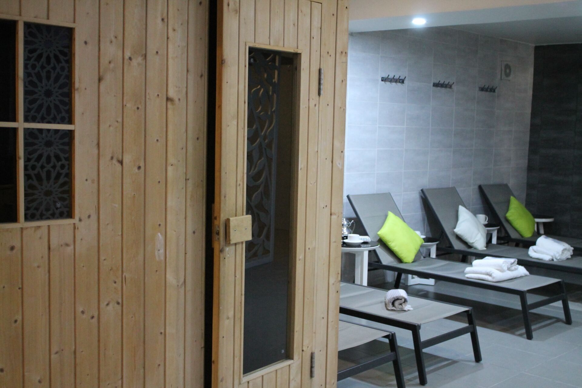 Un cuarto de spa con paredes de madera, zona de ducha con azulejos y varios sillones de descanso con toallas y almohadas.