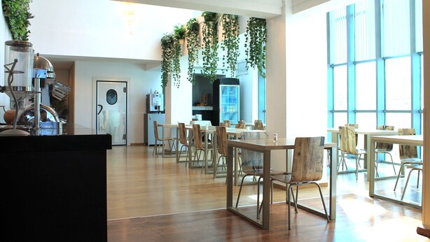 A spacious dining area with wooden tables and chairs, a kitchen area with a refrigerator and a coffee machine, and large windows providing natural light. - Palace Appart Hôtel (Algiers)