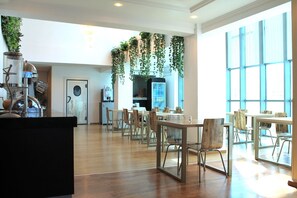 A spacious dining area with wooden tables and chairs, a kitchen area with a refrigerator and a coffee machine, and large windows providing natural light. - Palace Appart Hôtel (Algiers)