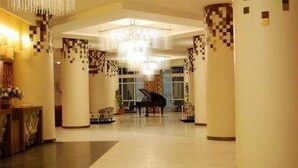 Een ruime lobby met een vleugelpiano, hoge plafonds en decoratieve zuilen.