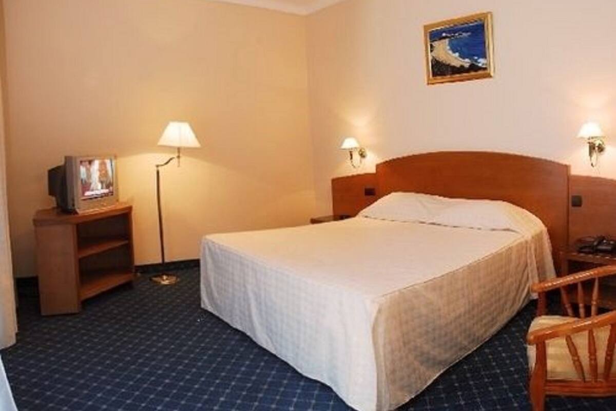 A hotel room with a bed, a small desk, a chair, and a picture on the wall.